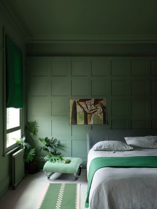 A green themed bedroom with wall panelling along the back wall