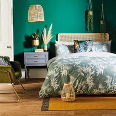 bedroom with green palm double duvet set beside drawer bed side table and woven lantern