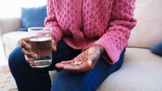 Gut health in winter - woman taking vitamin D capsule with a glass of water in her other hand