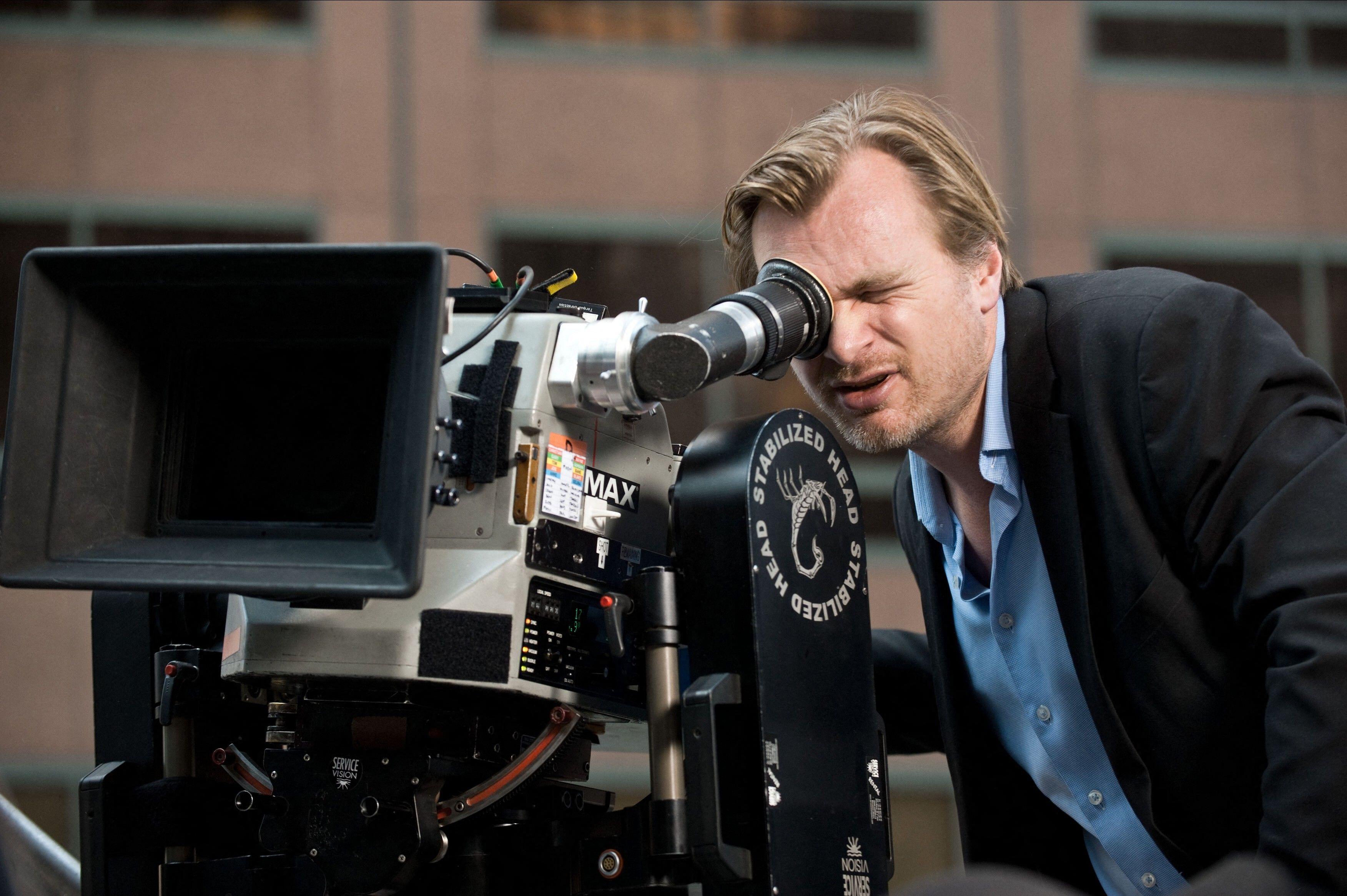 Christopher Nolan looking through the lens of a large film camera 