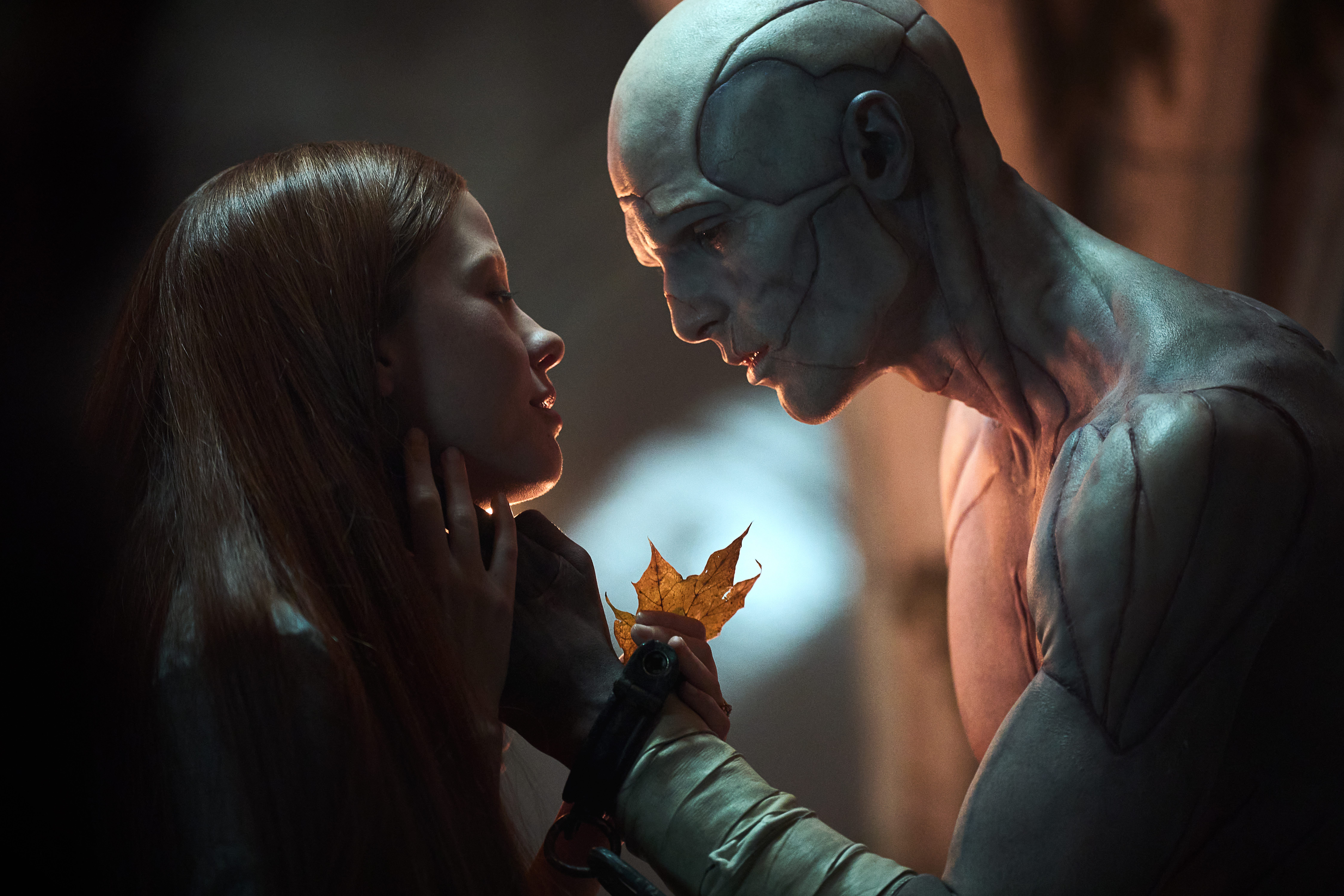 mia goth as elizabeth and jacob elordi as the creature holding a leaf and looking into each others' eyes in frankenstein