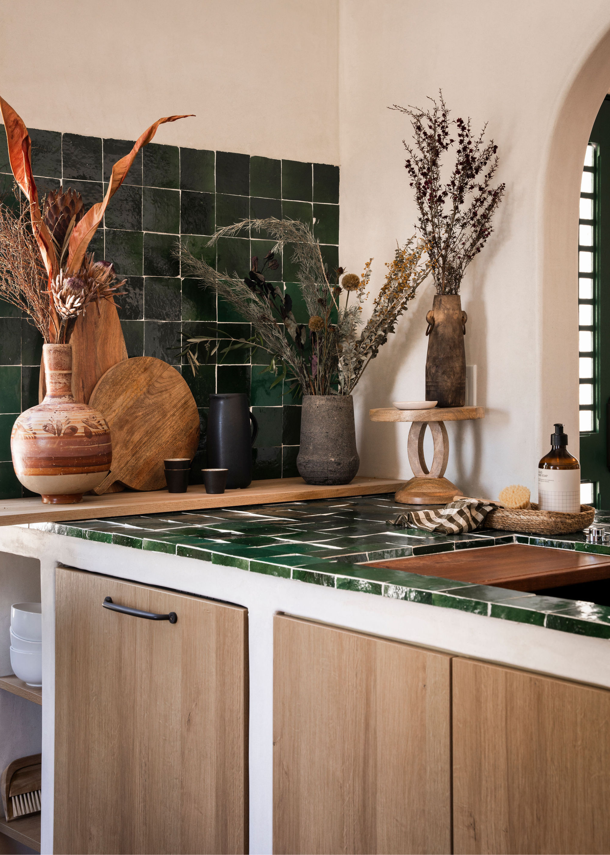 A small kitchen with dark green zellige tiles on the counter