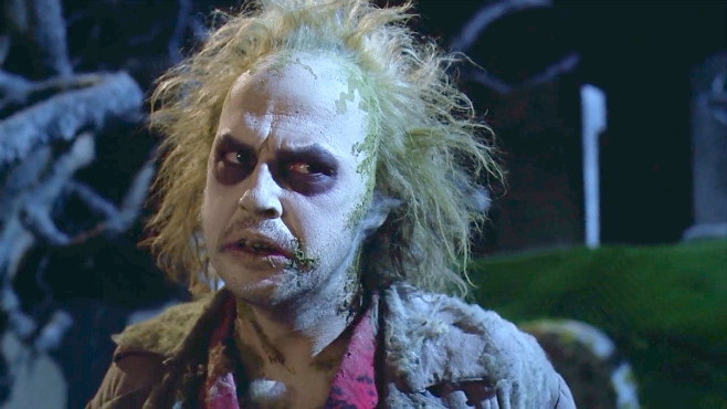 A still from the movie Beetlejuice showing the character Beetlejuice played by Michael Keaton wearing white makeup and black eye makeup.