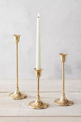 Three brass candlesticks with one white candle in the middle one