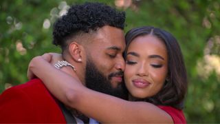 A close-up on Scotty and Aria's faces, close together as she wraps her arms around his shoulders, while they stand in front of green foliage, in 'The Ultimatum' season 3.