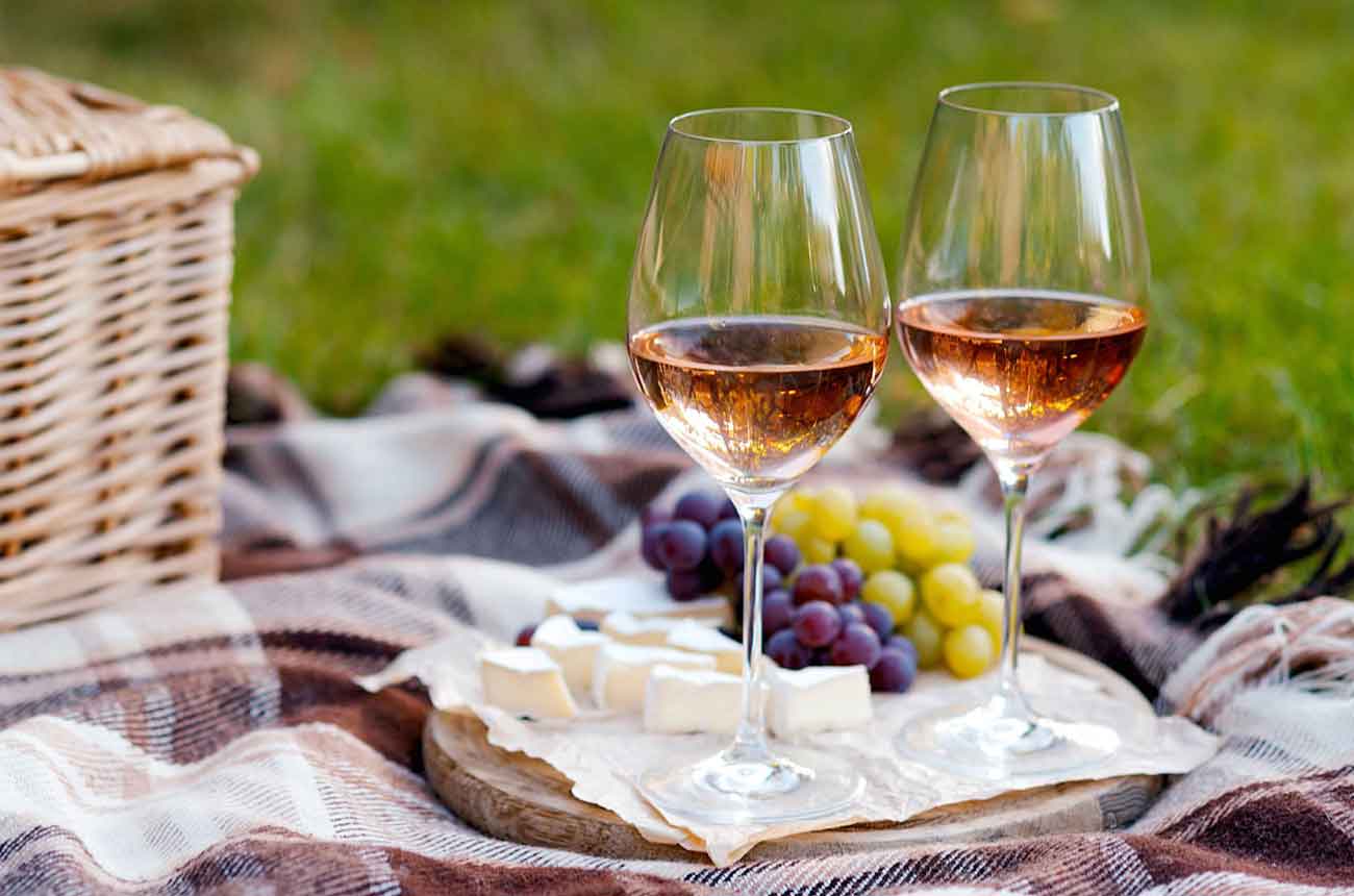 Two glasses of ros&eacute; wine with cheese and grapes on a plate in outdoor picnic scene