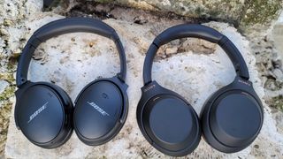 The Bose QuietComfort 45 and Sony WH-1000XM4 headphones next to each other, resting on a rock