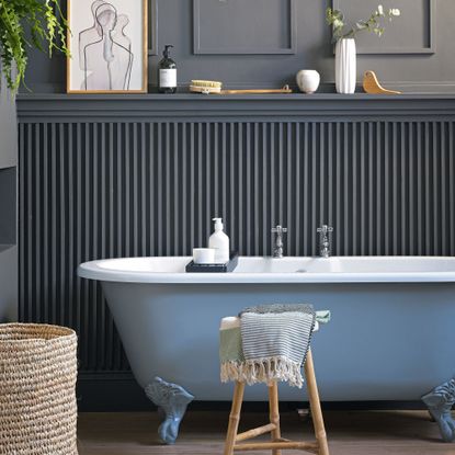 Freestanding bath in front of wooden panelled painted wall with decorative plants and towels in spa bathroom