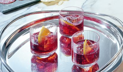 Marble top with 3 glasses of Negroni next to cold meat platter and flask of water