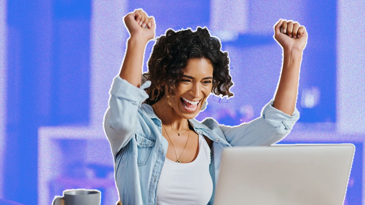 Young woman celebrating with arms in the air whilst sitting in front of computer