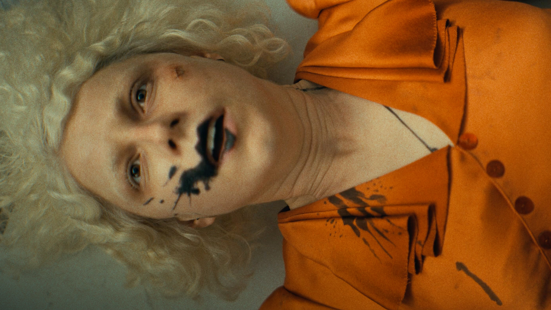 Jessie Buckley as the Bride, lying down with smudged black makeup and blonde hair