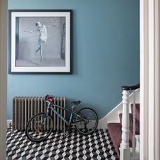 hallway with patterned tiled flooring and blue walls with a a bicycle leaning against a grey radiator 