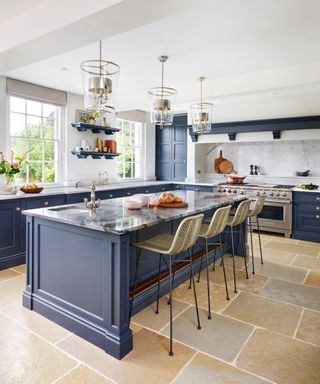 blue and white kitchen with blue cabinetry and kitchen island, bar stools, metal and glass trad lanterns above island,