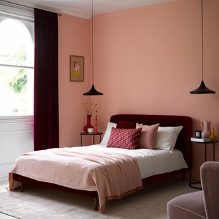 bedroom paint ideas, small bedroom colour ideas, coral bedroom with velvet claret bed and matching curtains, black pendant lights, red and pink accessories, artwork, black side tables, rug, armchair