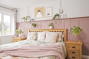 Bedroom with pink wall panelling, oak bed and bedside tables, white and brown themed artwork, floral and botanical bedding, and houseplants