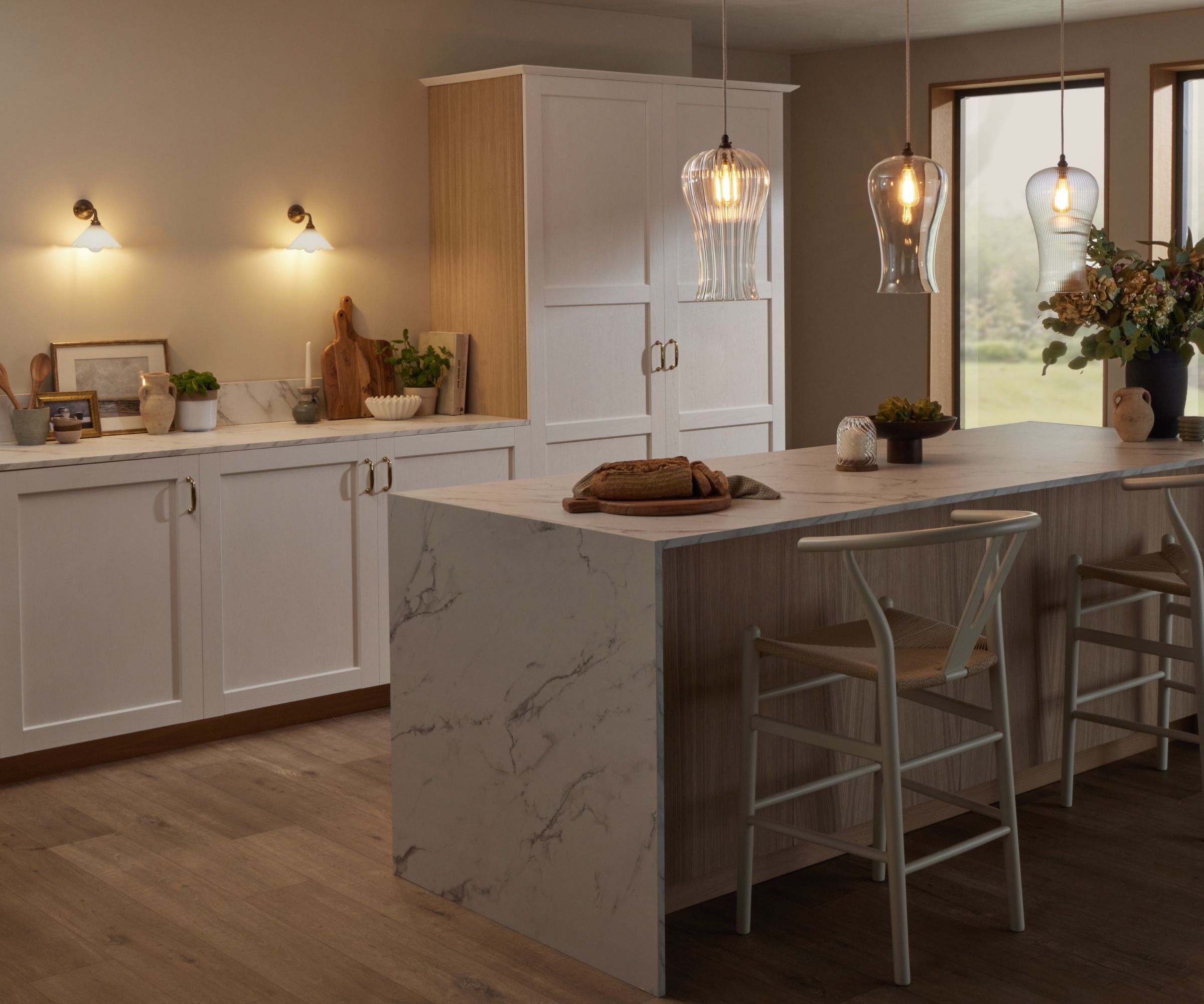 Modern white kitchen with marble island, glass pendant lights, wall sconces and bar stools, softly lit to create a warm, ambient atmosphere.