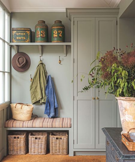 A functional mudroom area with sage green built-in cabinetry, a bench with wicker storage baskets underneath, and vintage tins on a high shelf.