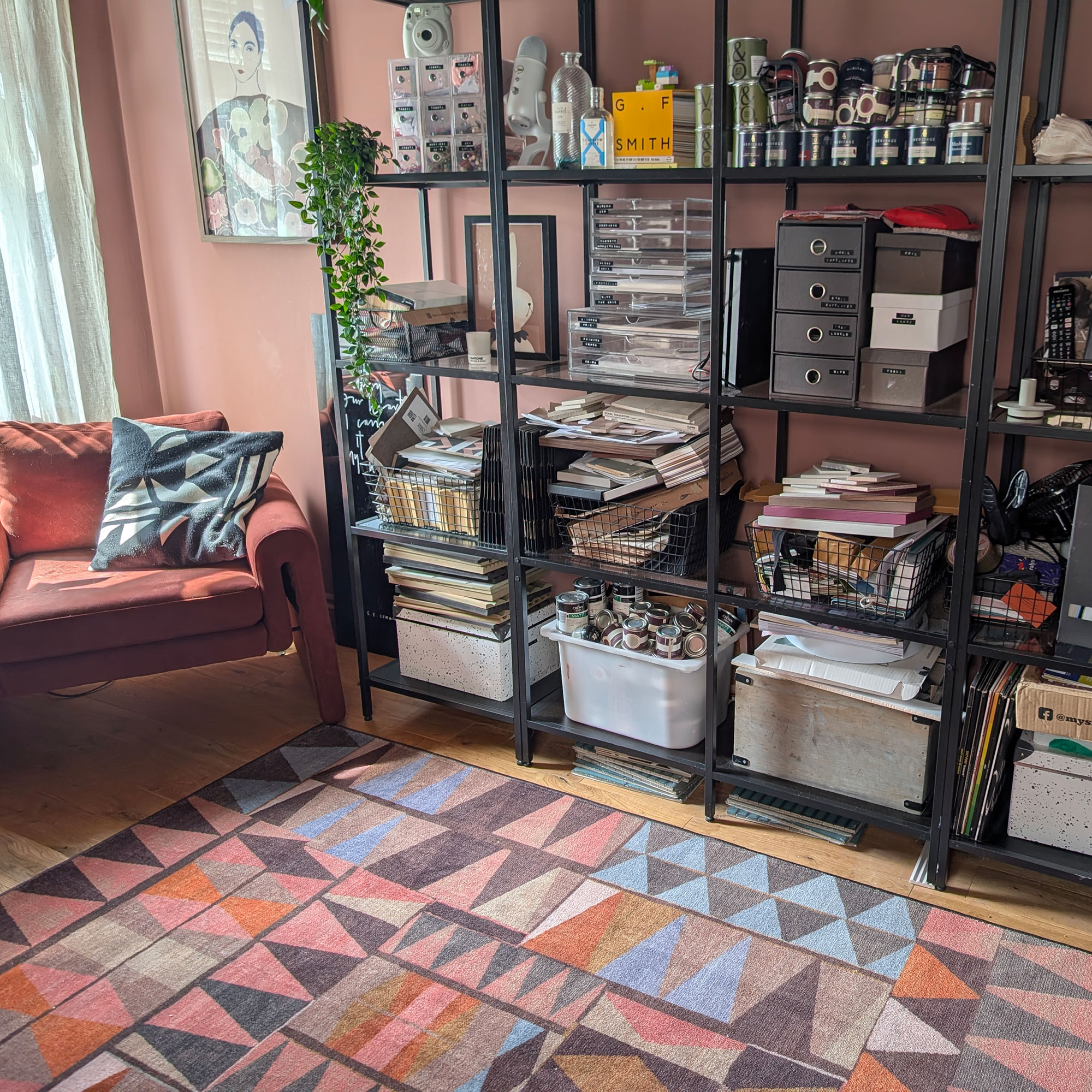 Home office space with industrial-style open shelving, orange-red armchair and rug with abstract pattern in pinks, browns, oranges and blues
