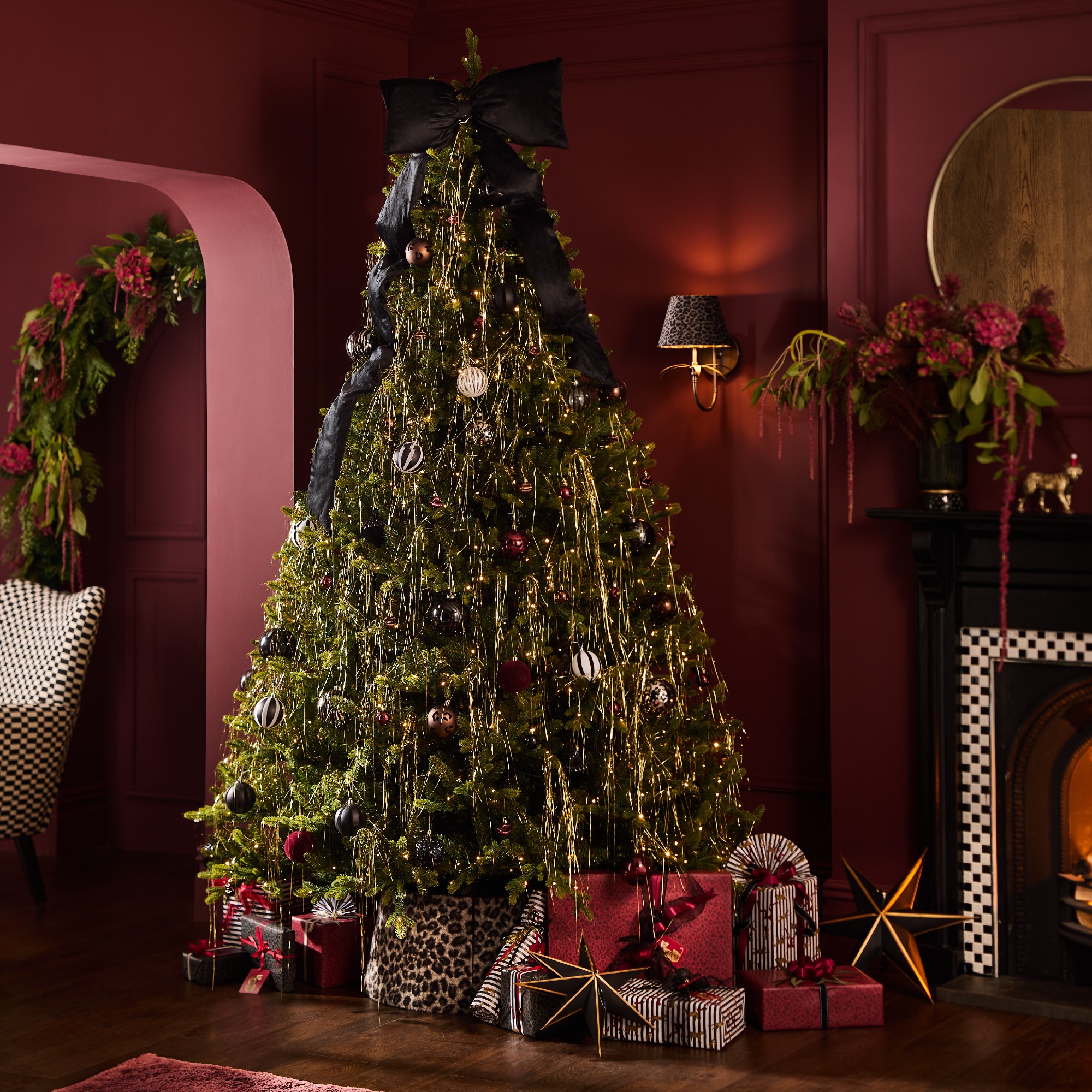 A dark-red painted room with a Christmas tree decorated with silver lametta and a large black bow tree topper