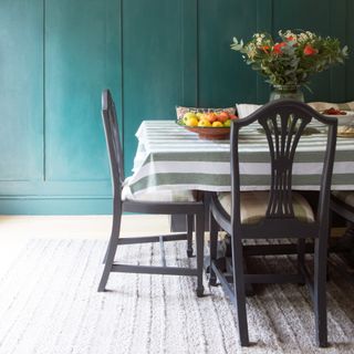 A dining room with a green panelled wall, a striped tablecloth and a light-coloured rug