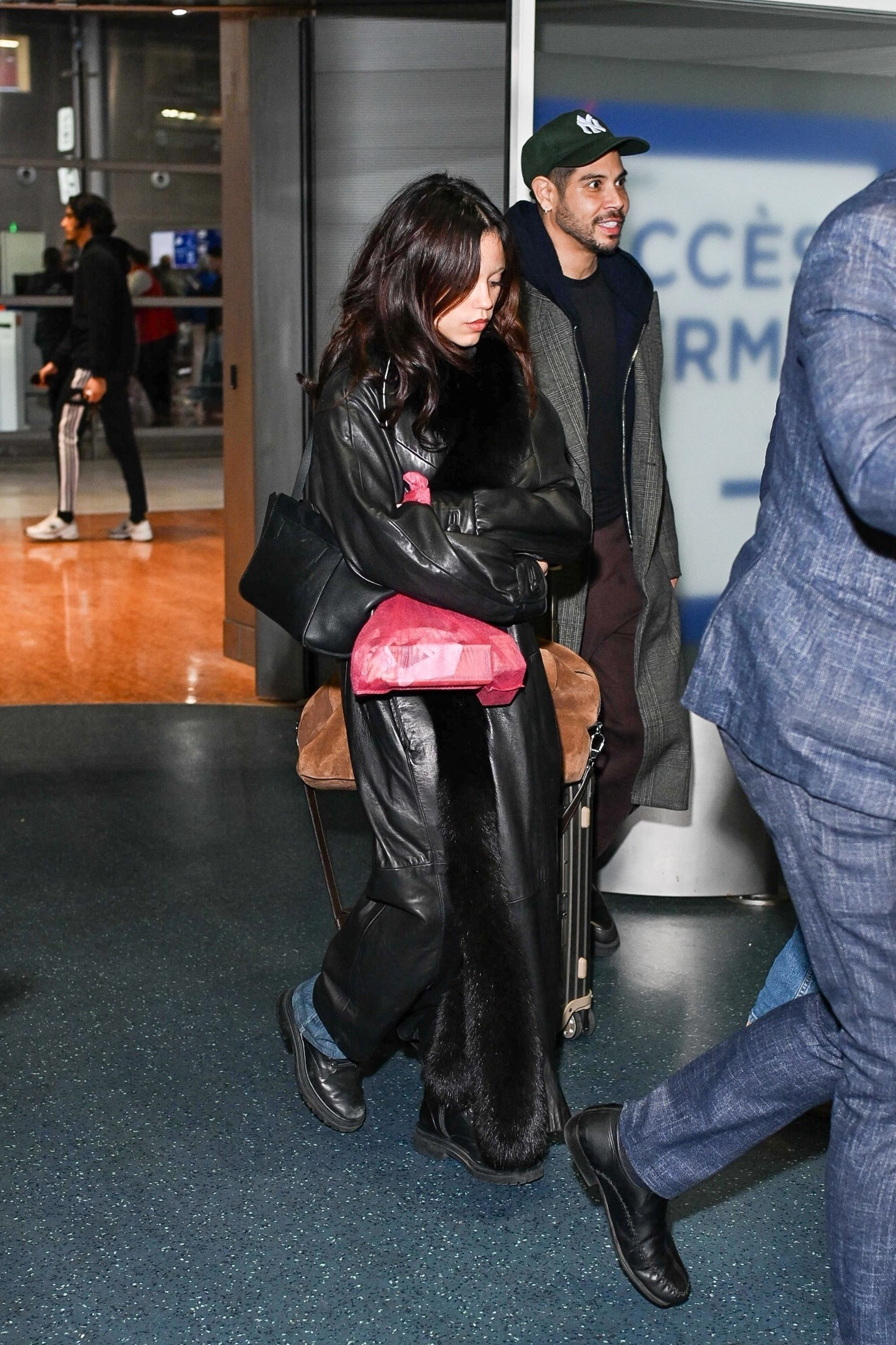 Jenna Ortega wearing a fur trim leather black coat, jeans, and black derby shoes