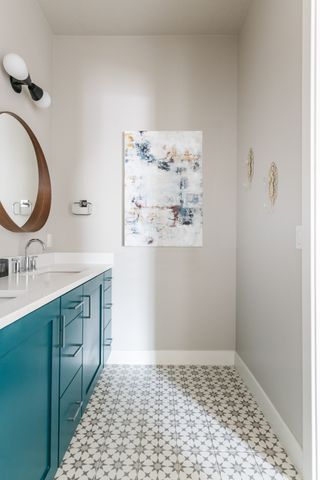 grey bathroom with teal vanity unit, wooden mirror, artwork, white countertop, star grey floor tiles