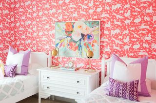 Bright pink animal wallpaper and simple, elegant white painted furniture, with floral wall art and purple and white bedlinen.