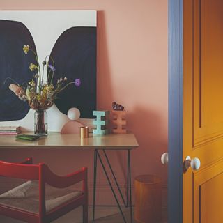 A pink-painted home office with a blue door and a red chair at the desk