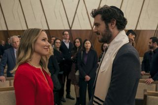 Kristen Bell as Joanne and Adam Brody as Rabbi Noah, standing in front of congregants at a synagogue, in episode 102 of Nobody Wants This.