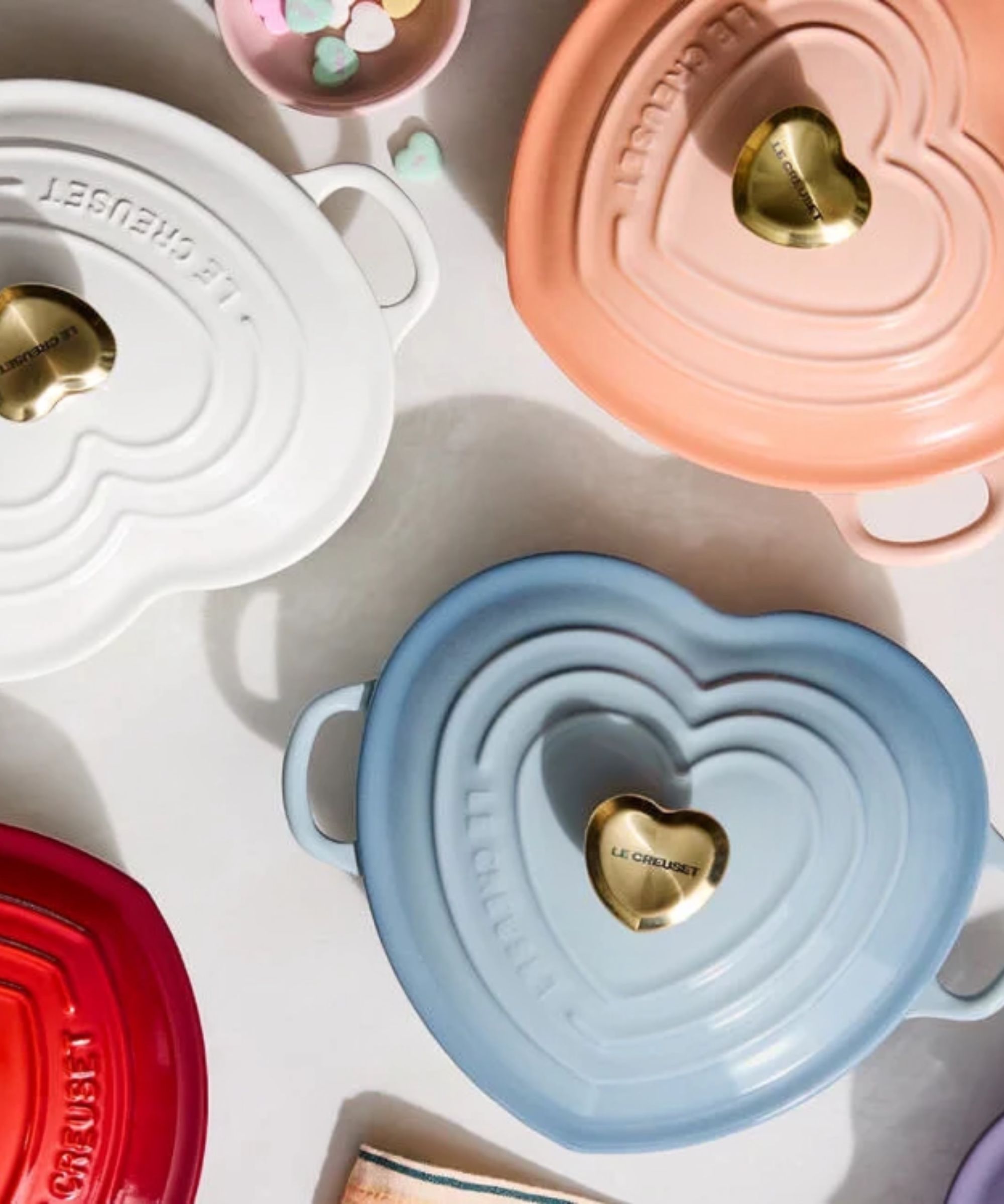 Three heart shaped cocette cooking pots with gold heart shaped lids in blue, white, and pink.