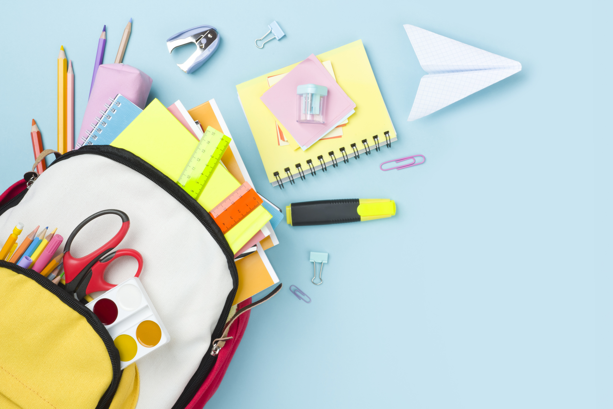 school supplies spilling out of a backpack on a blue background