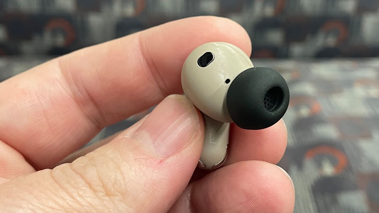 A hand holding a single JBL Tour Pro 3 earbud with the eartip visible.