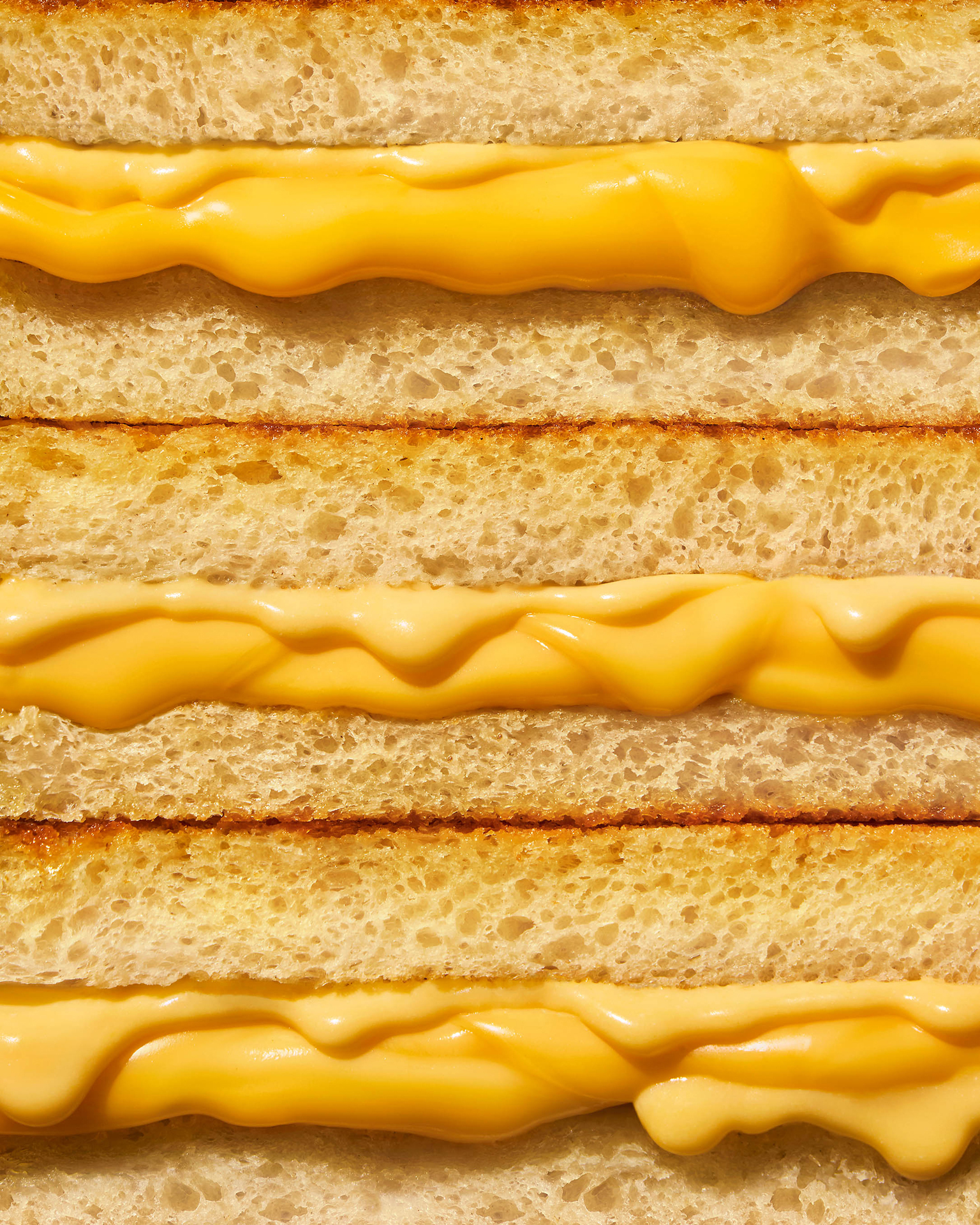 Close-up of three grilled cheese sandwiches in a row, with melted yellow cheese oozing between slices of golden-brown toasted bread