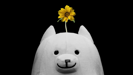 A plush dog has a sunflower sprouting from its head