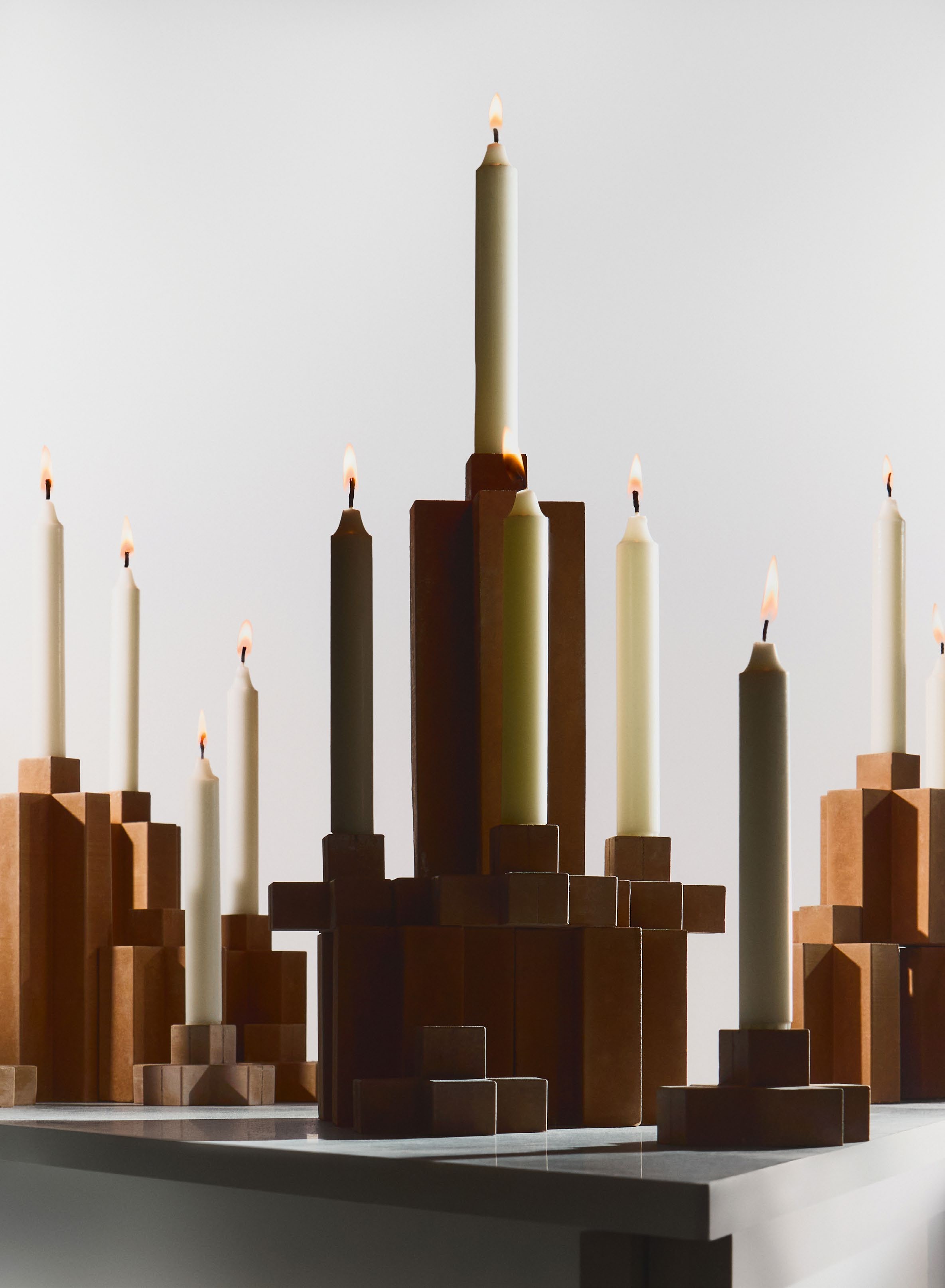 A modern candelabra arrangement featuring candles of varying heights, crafted from a geopolymer material inspired by discarded public sauna stones, highlighting Lennart Engels' innovative design.