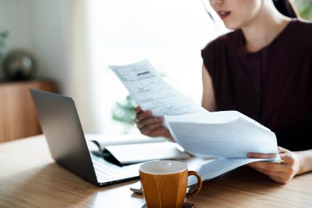 A woman sitting at dining table, handling personal finance with laptop. 