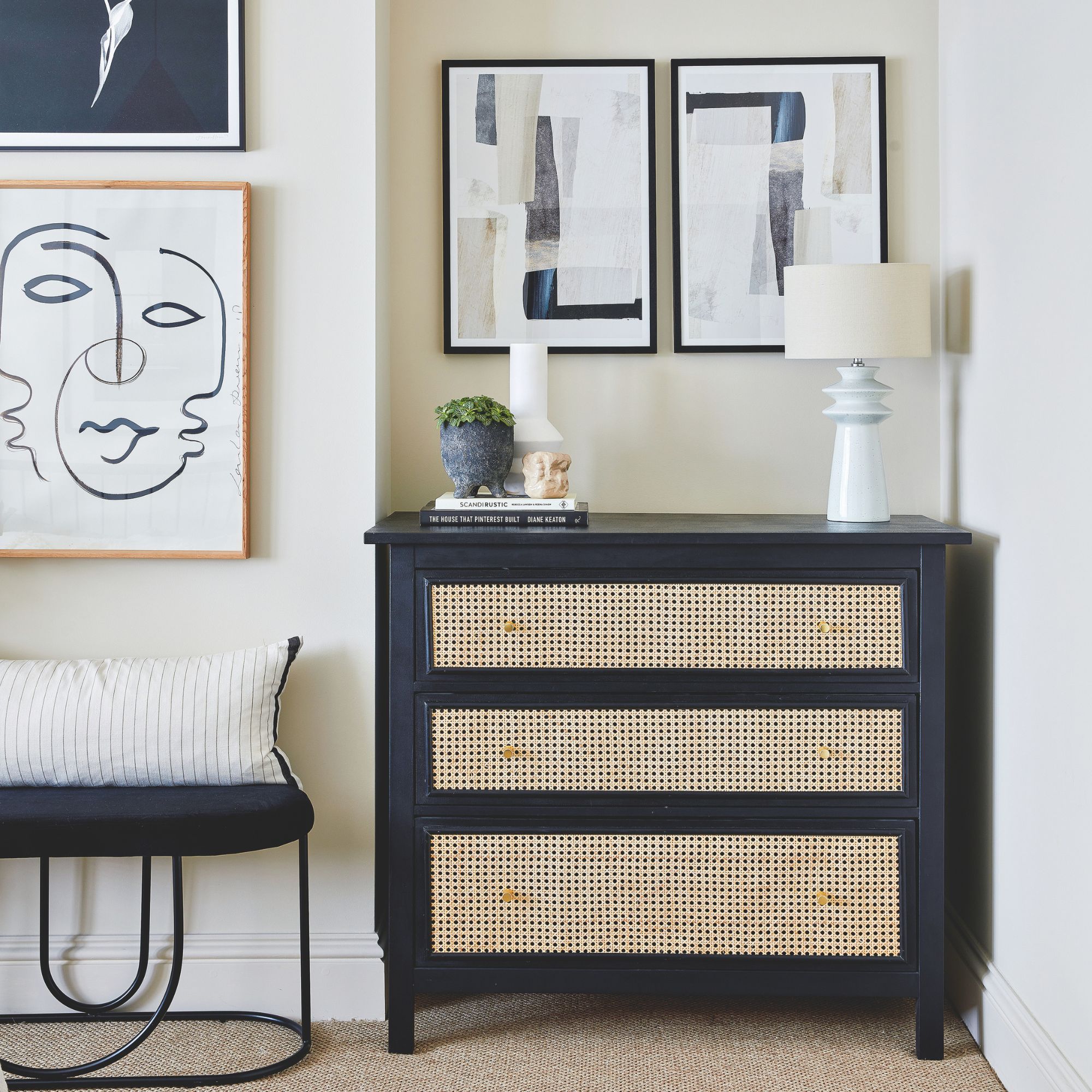 Black chest of drawers with rattan inserts against a white painted wall with artwork on the walls around it