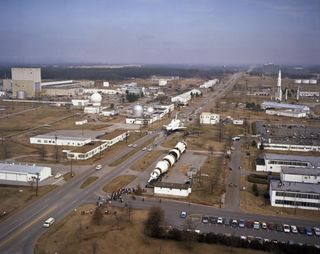 This March 15, 1978, photo of the George C. Marshall Space Flight Center shows the Space Shuttle Orbiter Enterprise being towed to the Dynamic Test Stand (not visible in photo) for vibration testing. It has just passed Building 4732, the Aero-Astrodynamics Laboratory, on its right. The tall building in the distance is Marshall’s main administrative office building.