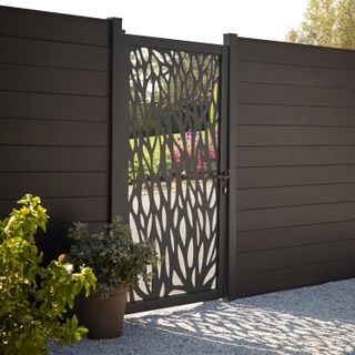 A dark brown paneled fence with ornate gate with a green garden beyond