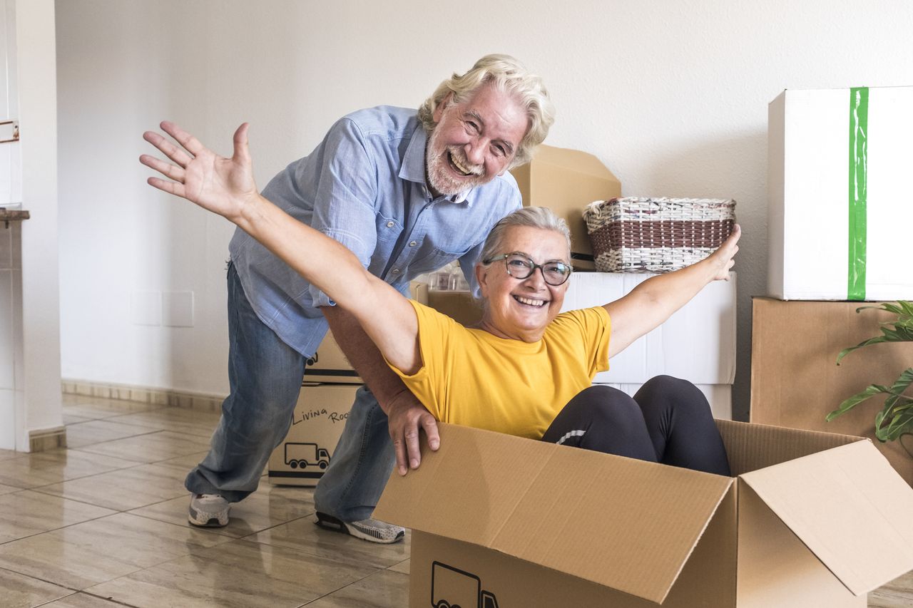 Happiness of two senior people in empty room playing like children in relocation happy for new beginning like retired with moving boxes on the floor