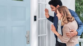 Two people standing outside door waving at Ring video doorbell