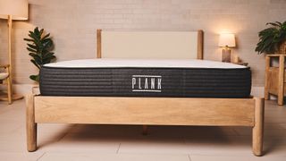 The foot of the Plank Firm mattress sitting on a wooden bed frame in a bedroom, showing the Plank logo