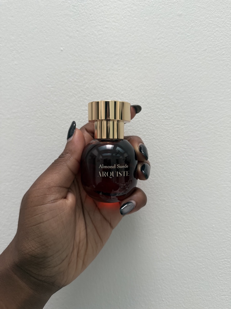 Maya Thomas holding a bottle of Arquiste's Almond Suede Eau de Parfum.