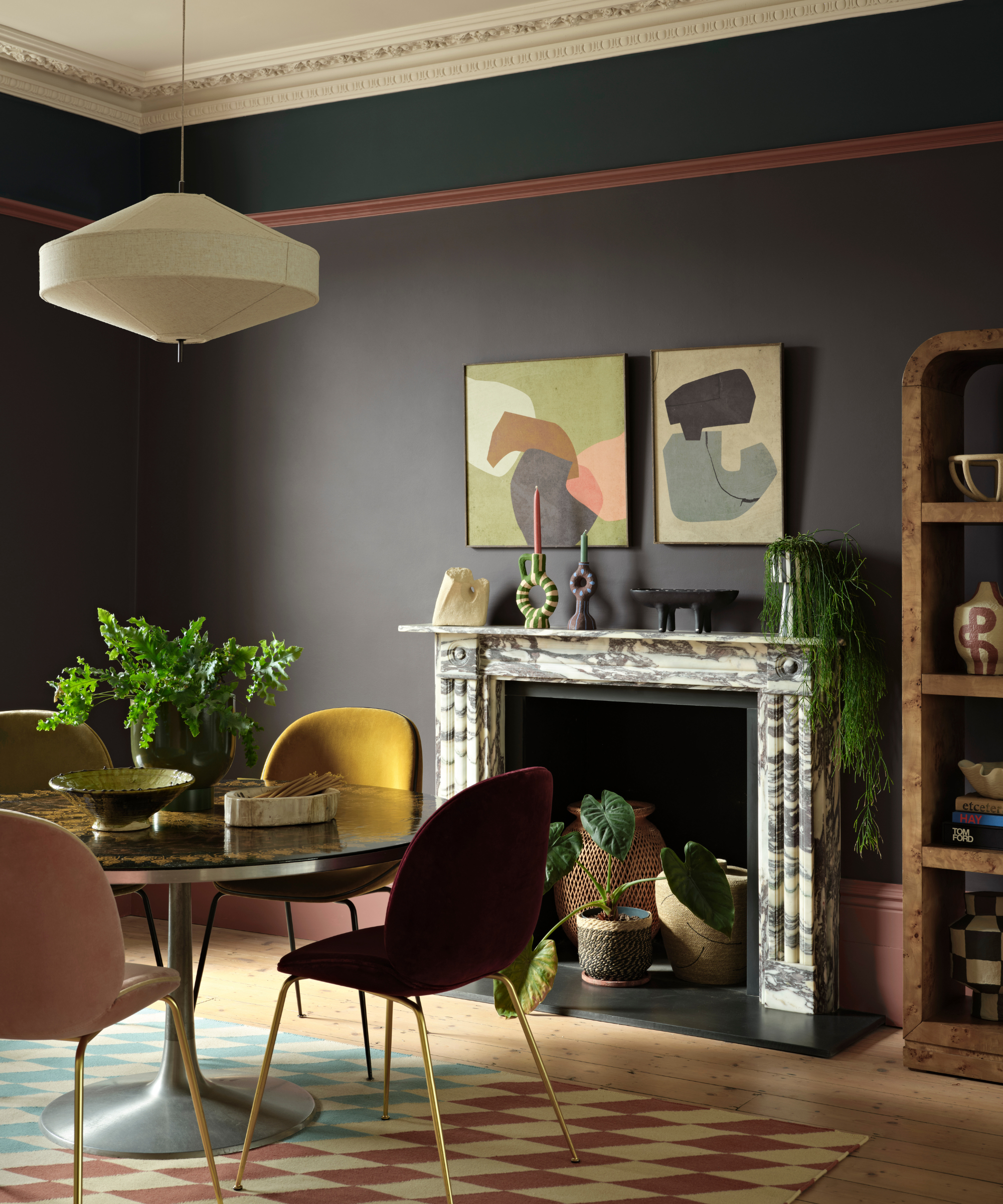 a dining room with a small round dining table with four colorful chairs, a fireplace made of marble with decorative objects on the mantel, a fabric pendant light hanging above the table, and walls painted with Benjamin Moore&#039;s Silhouette