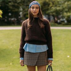 Woman in brown sweater, blue shirt, and check skirt