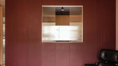 A kitchen with a red wall, a black chair and a reeded glass opening