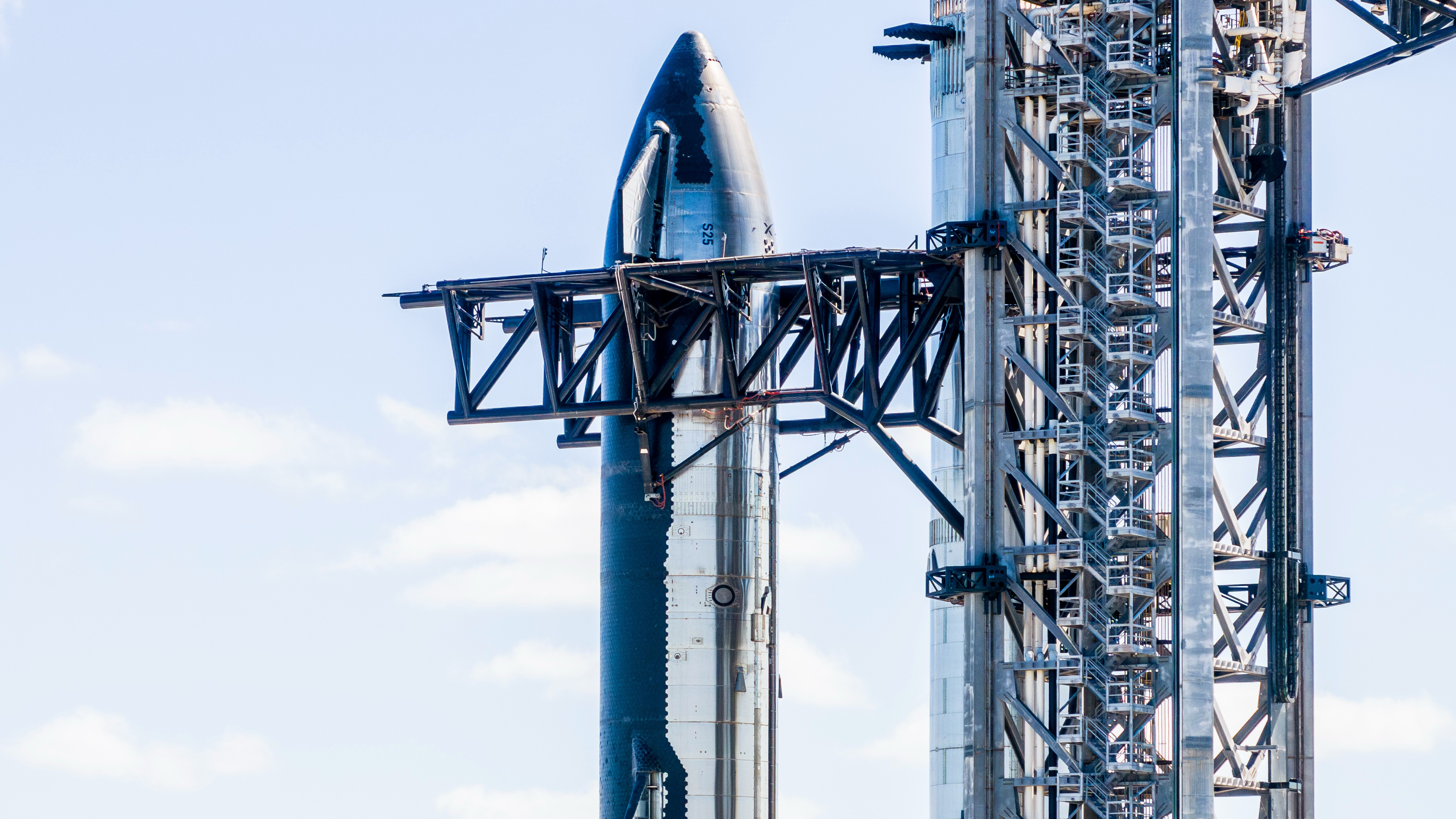 a shiny silver rocket is held by the arms of its gray launch tower.