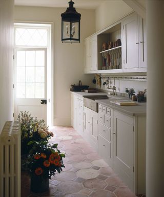 small plain english neutral galley kitchen along one wall with hexagon reclaimed terracotta floors