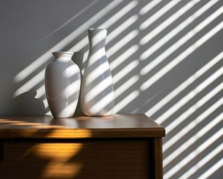 two white vases sat on a wooden side table against a white painted wall