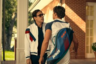 Javier Bardem as Jose Menendez, speaking with Nicholas Chavez as Lyle Menendez (who has a tennis racket bag on his back), in episode 201 of 'Monsters: The Lyle And Erik Menendez Story.'